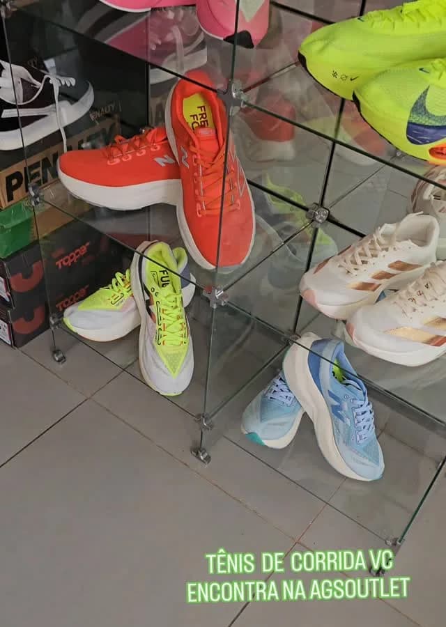 A vitrine de vidro da loja com os tênis de corrida: Nike laranja, New Balance e o Alphafly volt